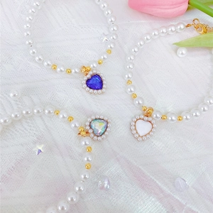 Detail of pearl pet necklace with heart sapphire pendants on white lace fabric background