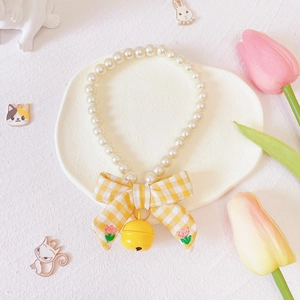 Close-up of pet pearl collar with a yellow plaid bow and a small gold bell charm