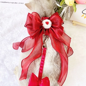 Detail view of red pet harness with organza bow, white fur ball and heart rhinestone