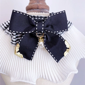 Detail of pet bowtie collar featuring black ribbon, plaid fabric, and pearl pendant