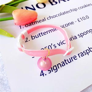 Detail of pink velvet pet collar featuring a pearl bell and white safety buckle