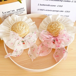 Detail of straw hats featuring cherry bow ties and satin ruffles on a wooden tray