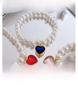 Detail of pearl pet necklace with heart-shaped gemstone pendants in blue, red, and pink