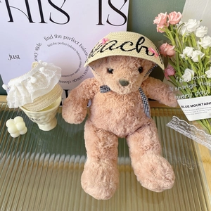 Detailed view of a teddy bear wearing a woven straw sun hat with pink bow and lace trim