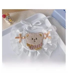 Detail of hand-knitted white pet bib with lace trim and cute brown teddy bear embroidery