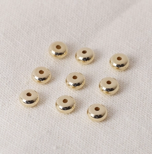 Detailed view of 9 golden CCB flat spacer beads for DIY jewelry making on soft fabric