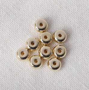Macro shot of nine golden CCB flat spacer beads with smooth metallic finish and center holes