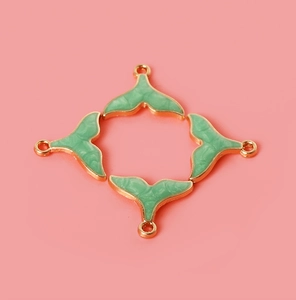 Close-up of four golden fish tail pendants with green marble enamel for DIY jewelry