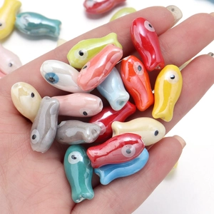 Hand holding colorful cartoon fish ceramic beads for DIY jewelry making and bracelets