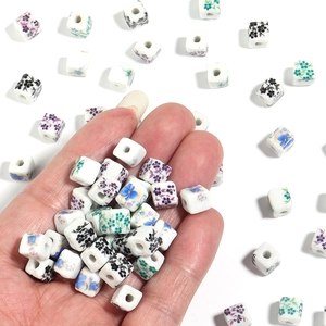 Macro shot of square white ceramic beads with colorful floral patterns for DIY jewelry