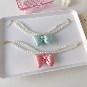 Detail of double-layer pearl pet collar with satin bow and heart crystal on a tray