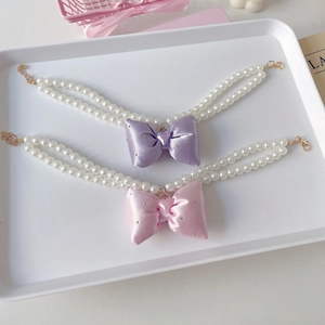 Close-up of double-layer faux pearl pet necklaces with purple and pink satin bows