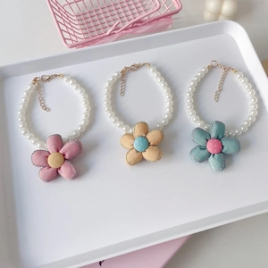 Close-up of three pearl pet necklaces with colorful fabric flower charms in a white tray