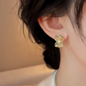 Detalle de elegantes pendientes de botón dorados con diseño de flores caladas y circonitas.