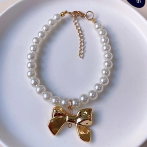 Detail view of pearl pet necklace with a shiny golden bow pendant and lobster clasp