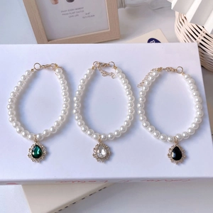 Detailed macro view of three pearl pet necklaces with emerald, clear, and black drop pendants