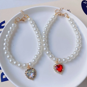 Detailed macro of heart pendants with rhinestones on pearl pet necklaces