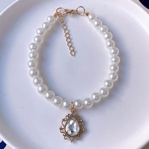 Macro view of imitation pearl pet necklace featuring a teardrop crystal pendant and gold clasp