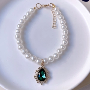 Detailed macro view of white pearl pet necklace with a green waterdrop gemstone pendant