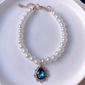 Macro shot of faux pearl pet necklace with water-drop blue gemstone and gold plating