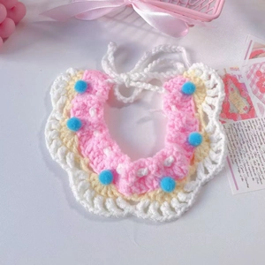 Macro detail of hand-knitted pet bib with blue pom-poms and adjustable white ties