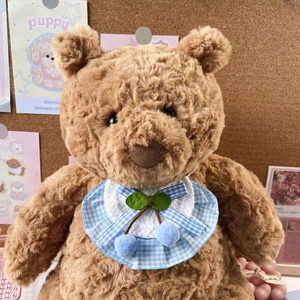 Close-up of brown teddy bear wearing a blue checkered pet bib with cherry pompoms