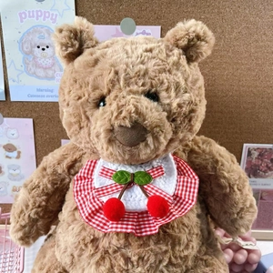 Detail of plush teddy bear wearing a red checkered bib with handmade crochet cherry decor