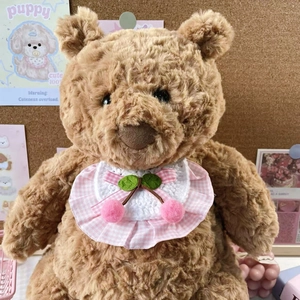 Detailed view of a brown teddy bear plush wearing a cherry themed crochet bib with lace edge
