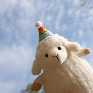 Gros plan d'un mouton en peluche blanc avec un chapeau de fête arc-en-ciel sur ciel bleu