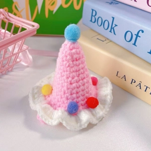 Close-up of a pink hand-knitted party hat for pets with colorful pom-poms and white frills