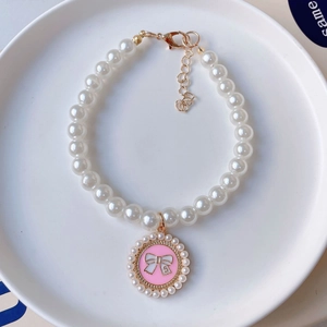 Detail of pet pearl necklace featuring a pink bow pendant and gold lobster clasp