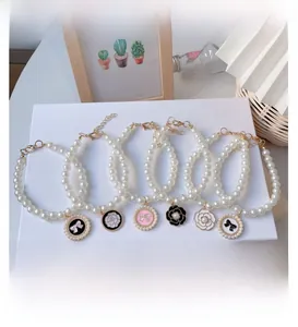 Detail of pearl pet collars with camellia and bow pendants on white gift box