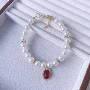 Close-up of pearl pet necklace with red gemstone pendant and gold plated accents