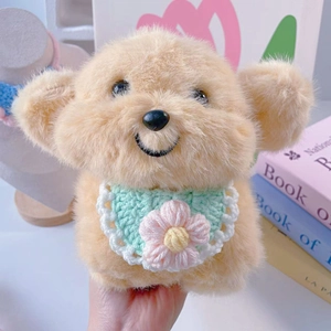 Close-up of cream teddy bear plush toy wearing a green hand-crocheted floral bib