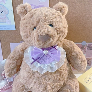 Dettaglio dell'orso di peluche con bavaglino in pizzo lavanda e fiocco viola