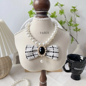 Detailed view of pearl cat collar with black and white plaid bow on a model stand