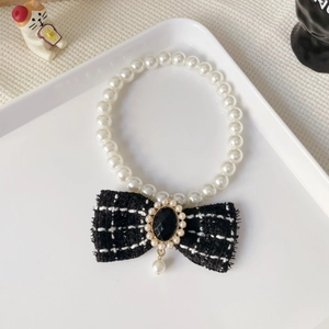 Close-up of pearl pet necklace featuring a black and white tweed bow with gold accents