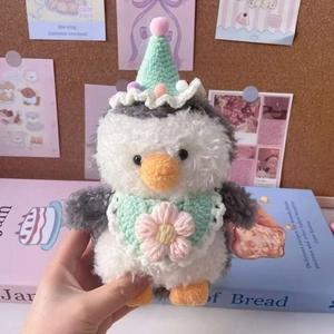 Close-up of penguin plush with mint green knitted hat and floral bib accessory