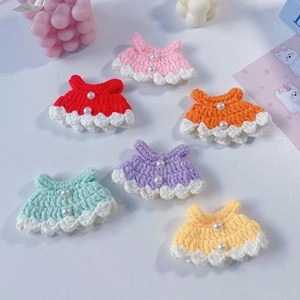 Detailed macro of six colorful handmade knit doll dresses with pearl buttons and ruffles
