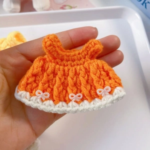 Detail of hand-crocheted orange 15cm doll dress with white bows and lace edges