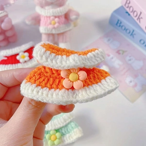Detail of hand-knitted striped doll dress with 3D floral accent in orange and cream
