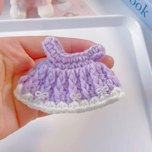 Detail of purple hand-knitted 20cm doll dress with white bows and pearl accents