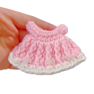 Pink handmade crochet doll dress with white bead bows shown in hand for scale