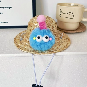 Macro detail of pet straw hat with blue pompom monster and adjustable elastic chin strap