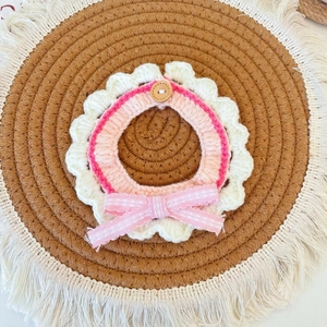 Detail of pink hand-knitted pet collar with lace bow and wooden button on woven mat