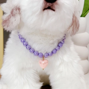 Detail of purple beaded pet necklace with pink heart pendant on a white dog