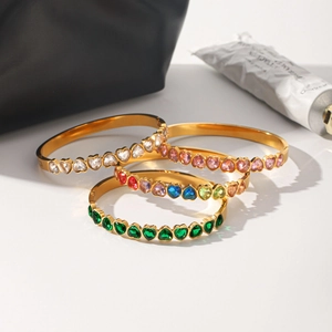 Gros plan de quatre bracelets en acier doré ornés de zircons colorés en forme de cœur