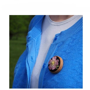 Borduurspeld met roze bloem en houten frame gedragen op een blauw vestje
