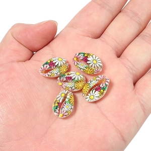 Close-up of hand holding hand-painted cowrie shells with daisy patterns for DIY jewelry