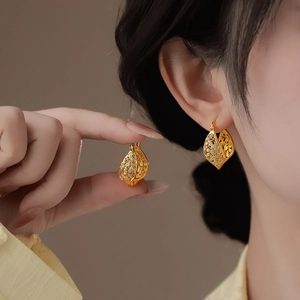 Détail de boucles d'oreilles créoles torsadées en filigrane d'or portées par un modèle.